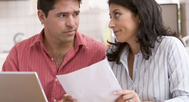 Couple in kitchen with paperwork using laptop look