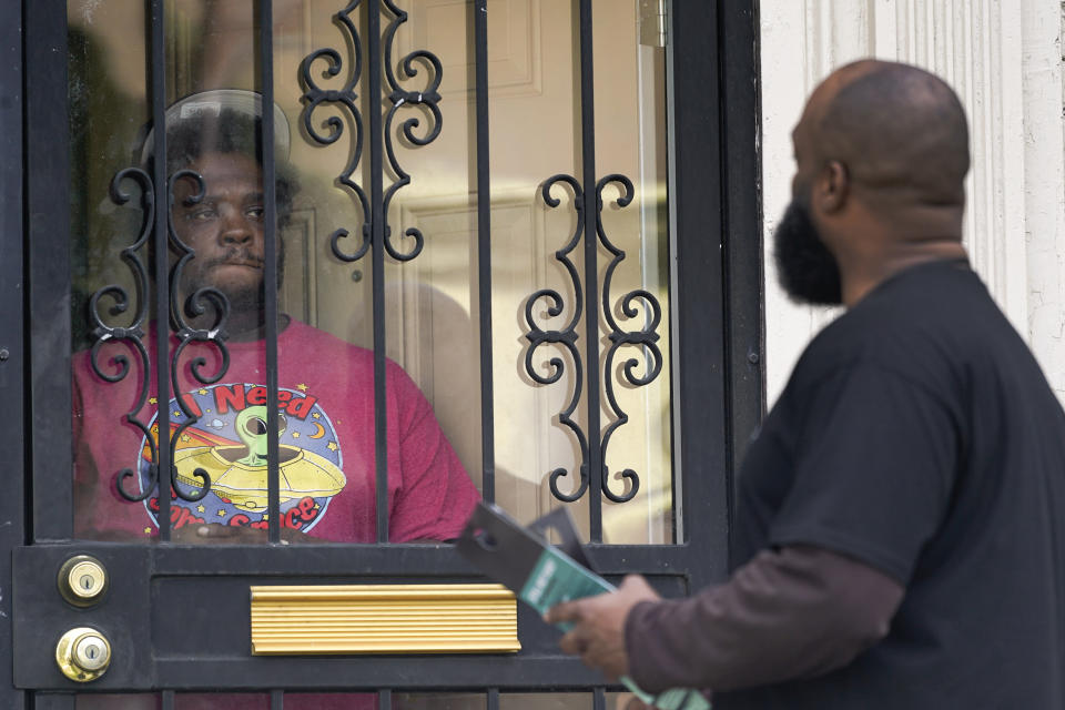 Anthony Brinson, right, talks with a resident while leaving a flyer at a home in Detroit, Tuesday, May 4, 2021. Officials are walking door-to-door to encourage residents of the majority Black city to get vaccinated against COVID-19 as the city's immunization rate lags well behind the rest of Michigan and the United States. (AP Photo/Paul Sancya)