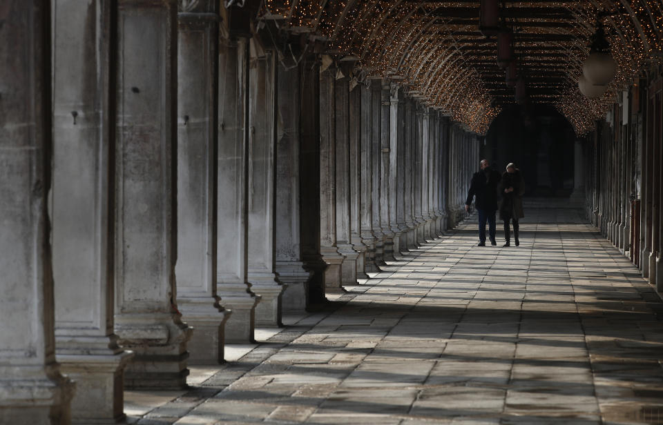 People walk down a passageway near St. Mark's Square in Venice, Italy, Saturday, Jan. 30, 2021. Gondolas and other vessels are moored instead of preparing for Carnival's popular boat parade in the lagoon. Alleys are eerily empty. Venetians and the city's few visitors stroll must be masked in public places, indoors and out, under a nationwide mandate. (AP Photo/Antonio Calanni)