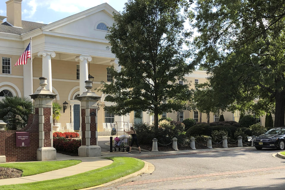 A woman rolls her belongings into the Ernest F. Hollings National Advocacy Center at the University of South Carolina on Wednesday, Sept. 2, 2020, in Columbia, S.C. The university ran out of space at a dormitory for quarantined students and began sending them to rooms it rented in hotel-like quarters at a training center for prosecutors. (AP Photo/Jeffrey Collins)