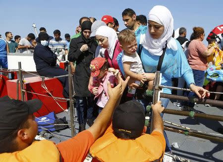Members of the Turkish coast guards help a Syrian migrant family to disembark on the shore in Cesme, near the Aegean port city of Izmir, Turkey, August 11, 2015. REUTERS/Osman Orsal
