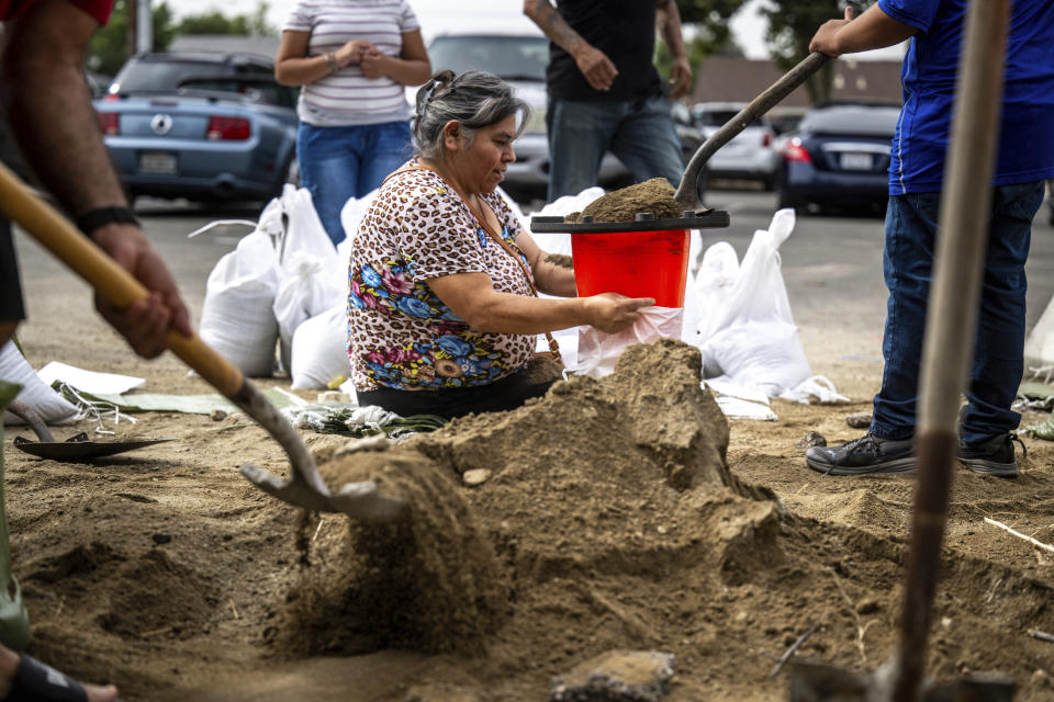 Sitting on the ground, Norma Panilla attentively fills sandbags at Wildwood Park in San Bernardino, Ca., on Saturday, Aug. 19, 2023, as she readies her home for potential floodwaters in anticipation of Hurricane Hilary's impending arrival. (Watchara Phomicinda/The Orange County Register via AP)