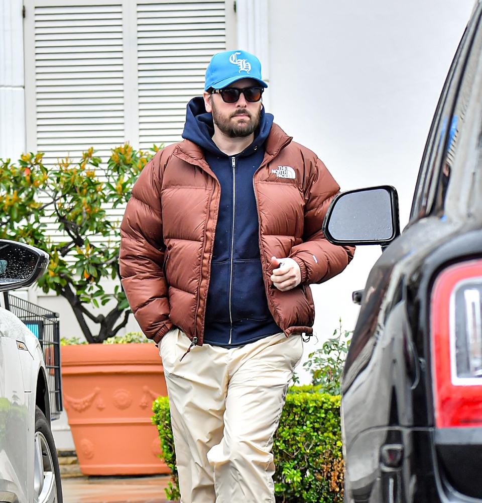 Close-up of Scott in a cap, sunglasses, and puffy jacket near a car