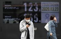 Passersby, wearing face masks due to the outbreak of the coronavirus disease (COVID-19), walk past a screen counting down the days to the Tokyo 2020 Olympic Games in Tokyo