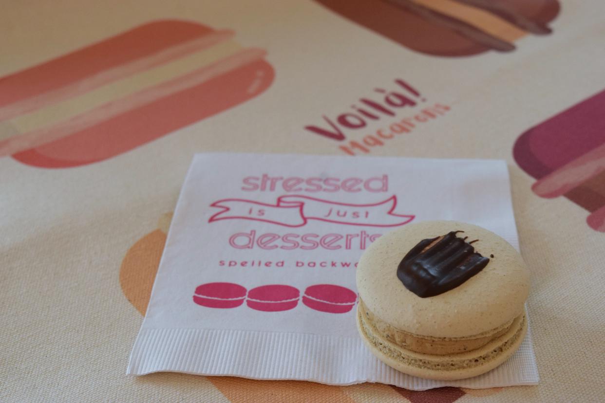 A mocha flavored Macaron sits on a napkin at Voilà! Macarons. In the background is a tote bag designed specifically for the shop.