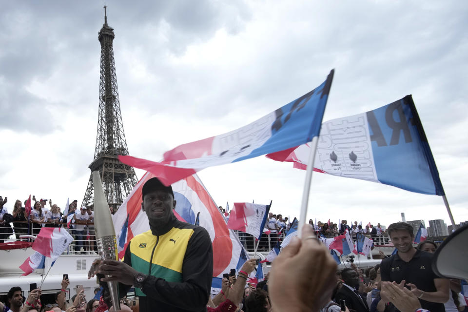 Tony Estanguet (derecha) - presidente del Comité Organizador de los Juegos Olímpicos de París 2024, y el exatleta jamaiquino Usain Bolt asisten a la ceremonia de la antorcha olímpica en París. Martes 25 de julio de 2023. (AP Foto/Christophe Ena)