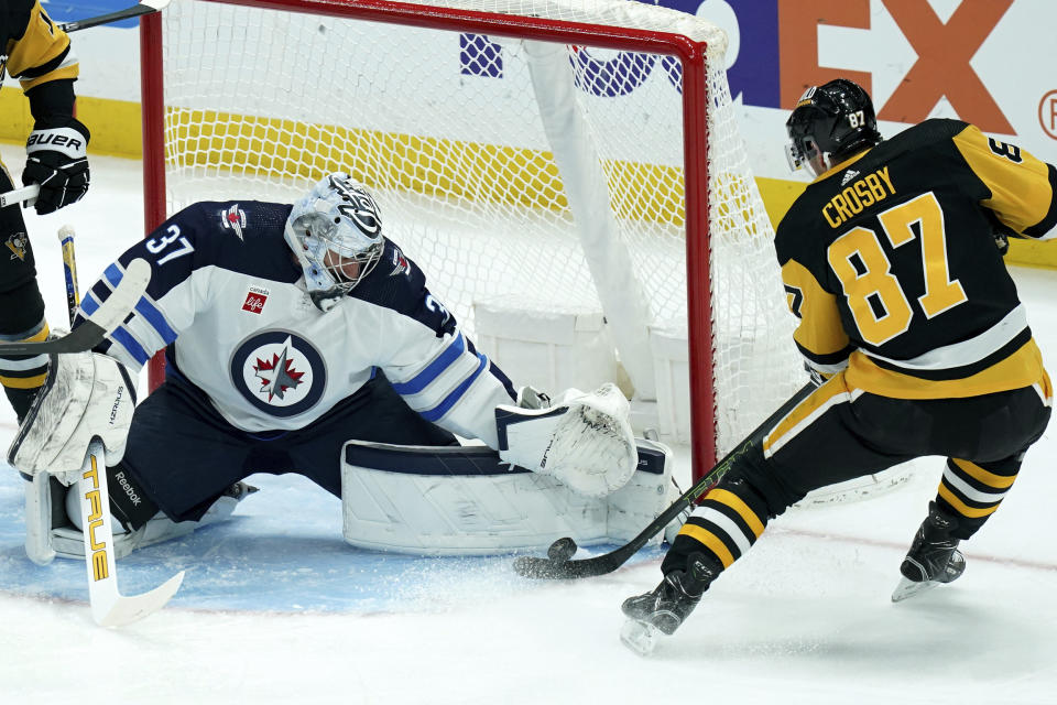 Winnipeg Jets goaltender Connor Hellebuyck (37) reaches to stop a shot by Pittsburgh Penguins Sidney Crosby (87) during the first period of an NHL hockey game, Tuesday, Feb. 6, 2024, in Pittsburgh. (AP Photo/Matt Freed)