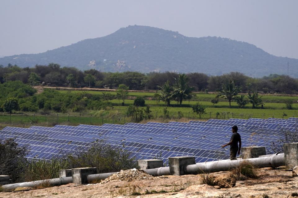 A man walks near a solar plant, an Adani Group project, in Ramanapeta, in the Indian southern state of Telangana, Wednesday, March 22, 2023. Gautam Adani and his companies lost tens of billions of dollars and the stock for his green energy companies have plummeted. Despite Adani's renewable energy targets accounting for 10% of India's clean energy goals, some analysts say Adani's woes won't likely hurt India's energy transition. (AP Photo/Mahesh Kumar A.)