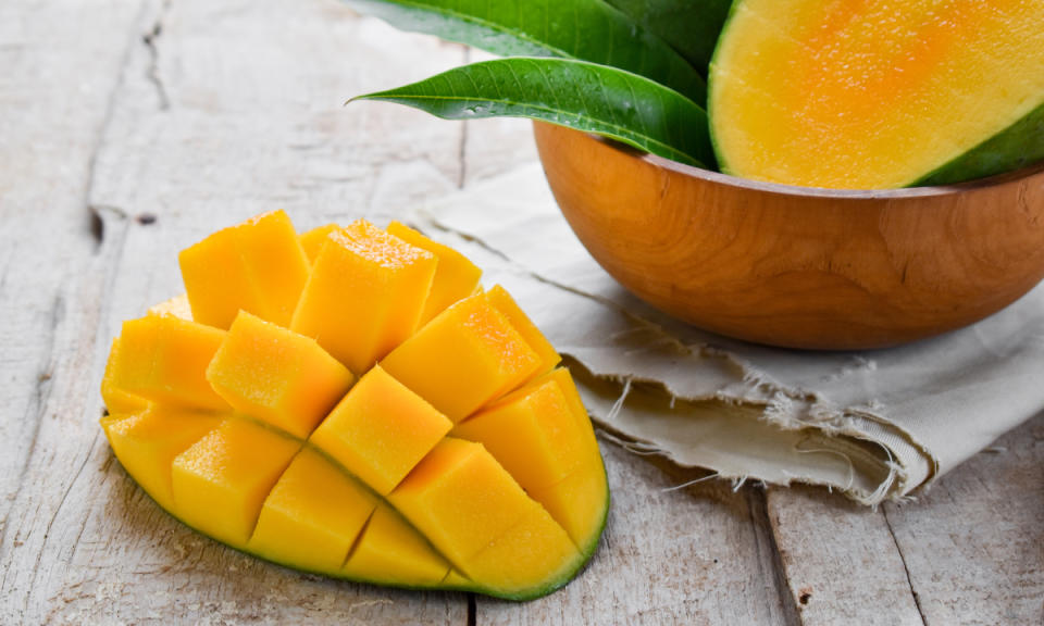 A diced mango beside a bowl of mangoes, which are good for constipation