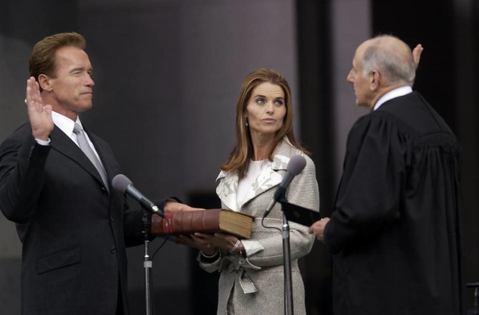 Arnold Schwarzenegger raises his hand as he takes the oath of office on Nov. 17, 2003, with California Supreme Court Chief Justice Ronald George as Maria Shriver holds a Kennedy family bible.