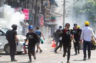 Tear gas and fire extinguisher gas float around demonstrators as they run away from police during a protest against the military coup in Yangon