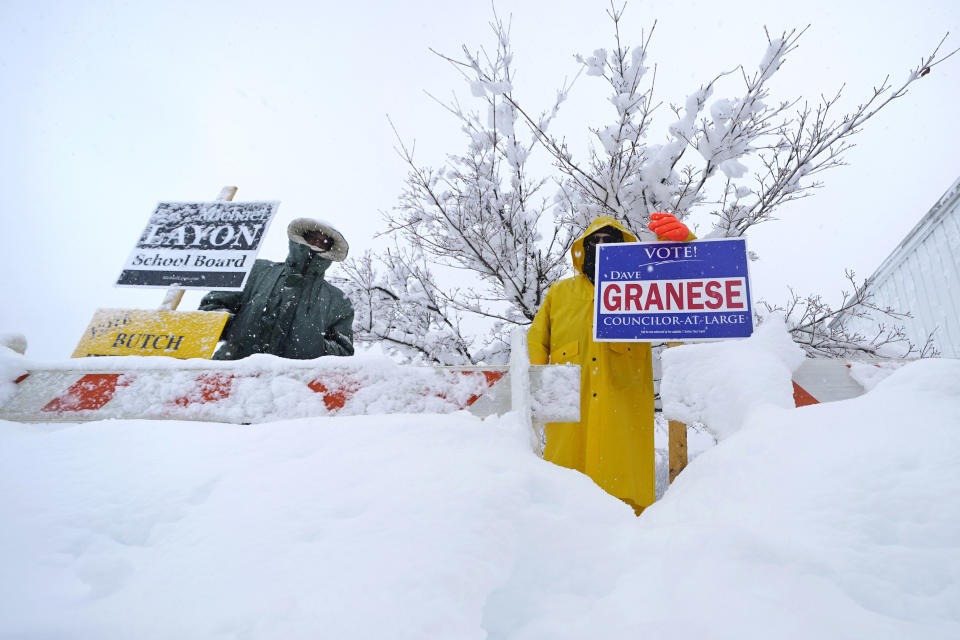 Michael Layon, left, a school board candidate, stands with Dave Granese, a councilor-at-large candidate, stand in a snow bank while campaigning on Election Day, Tuesday, March 14, 2023, in Derry, N.H. By the time the winter storm wraps up Wednesday, snow totals in New England are expected to reach a couple of feet of snow in higher elevations to several inches along the coast. (AP Photo/Charles Krupa)
