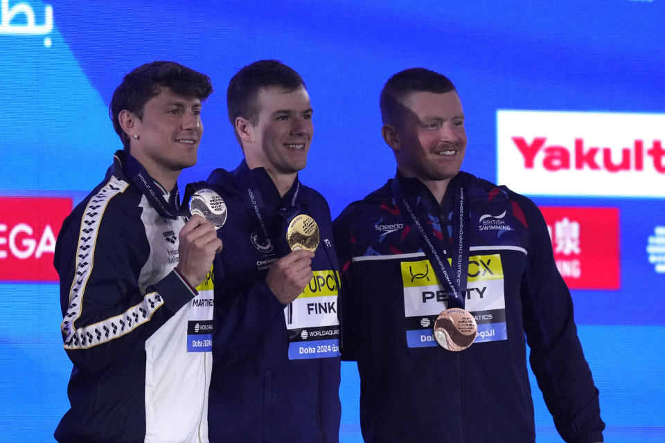 Gold medalist Nic Fink of the United States, center, silver medalist Nicolo Martinenghi of Italy and Adam Peaty of Britain pose for a photo during the medal ceremony for the men's 100-meter breaststroke final at the World Aquatics Championships in Doha, Qatar, Monday, Feb. 12, 2024. (AP Photo/Lee Jin-man)