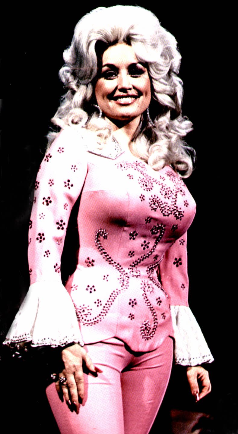 <p>Dolly Parton was rocking the pantsuit long before it was cool, and one of her first takes on the ensemble is classic Dolly: bell sleeves, floral embellishments, and Barbie pink with a pair of oversize hoop earrings..</p>