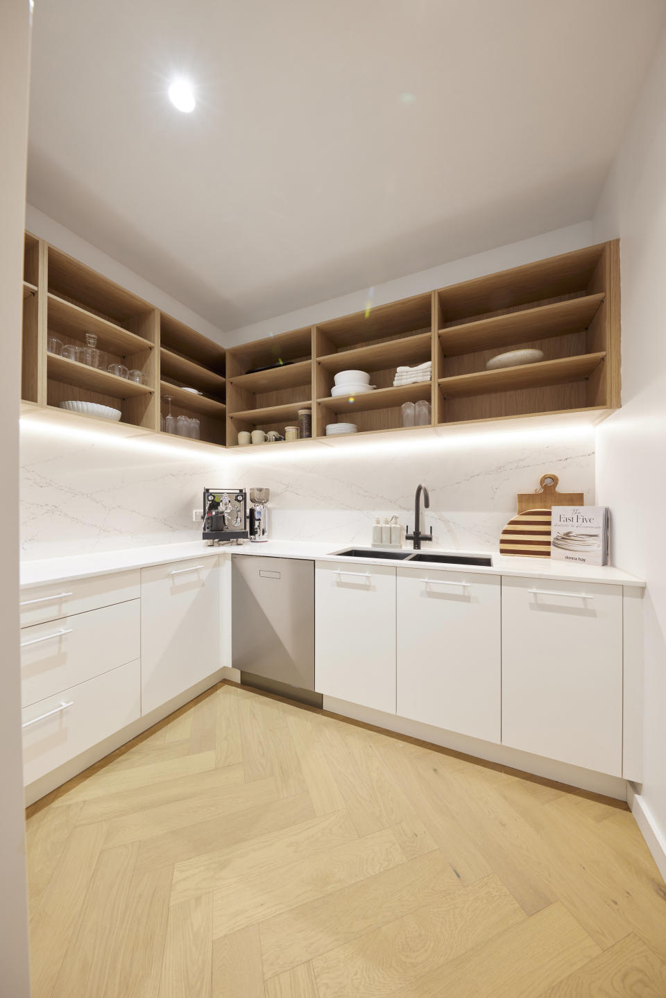 A wide shot of a pantry, with brown shelves along the top and wide cupboards 