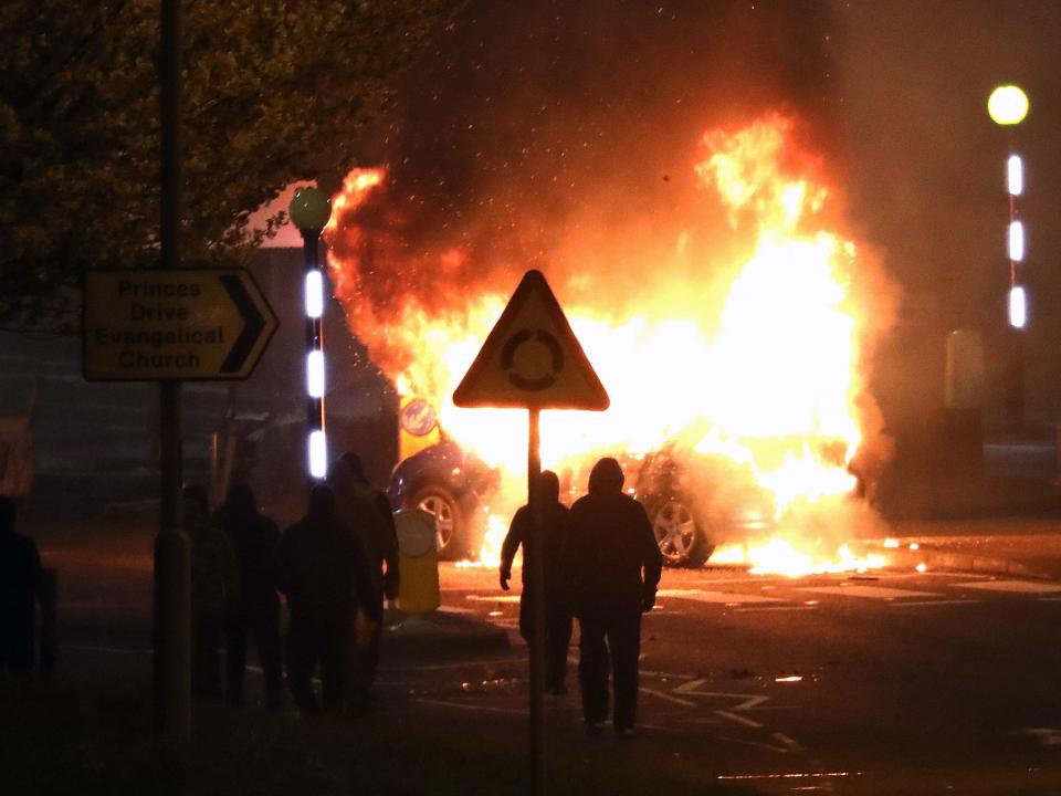 People walk past a burning car that was hijacked by loyalists at the Cloughfern roundabout in NewtownabbeyPeter Morrison/PA