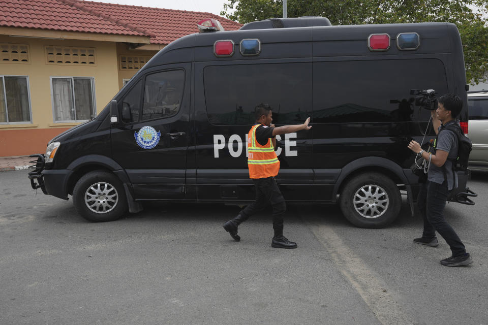 An airport security officer, left, tries to prevent journalists from filming a police convoy that was reportedly carrying Japanese citizens who were taken into custody on suspicion of running phone scams at Phnom Penh International Airport in Phnom Penh, Cambodia, Tuesday, April 11, 2023. Over a dozen of Japanese men detained in Cambodia in January on suspicion of taking part in phone and online scams were deported to their homeland on Tuesday, police said. (AP Photo/Heng Sinith)