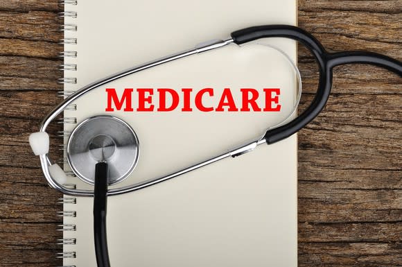 Spiral-bound notebook with red Medicare printed on it, with a stethoscope lyingon top of it on a wood table.