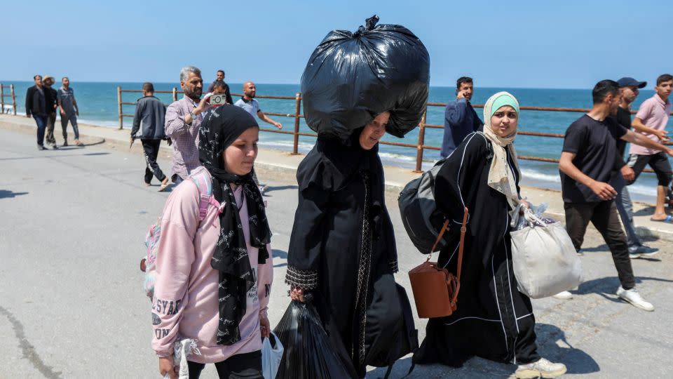 Um Mohammad (center) walks along the road carrying a heavy bag on her head and two others in her arms as she walks towards northern Gaza on April 14, 2024. - Ramadan Abed/Reuters