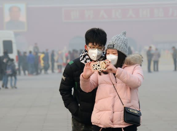 Tourists wearing face masks take a selfie on the Tiananmen Square in heavy smog in Beijing, China, Dec. 24, 2015.