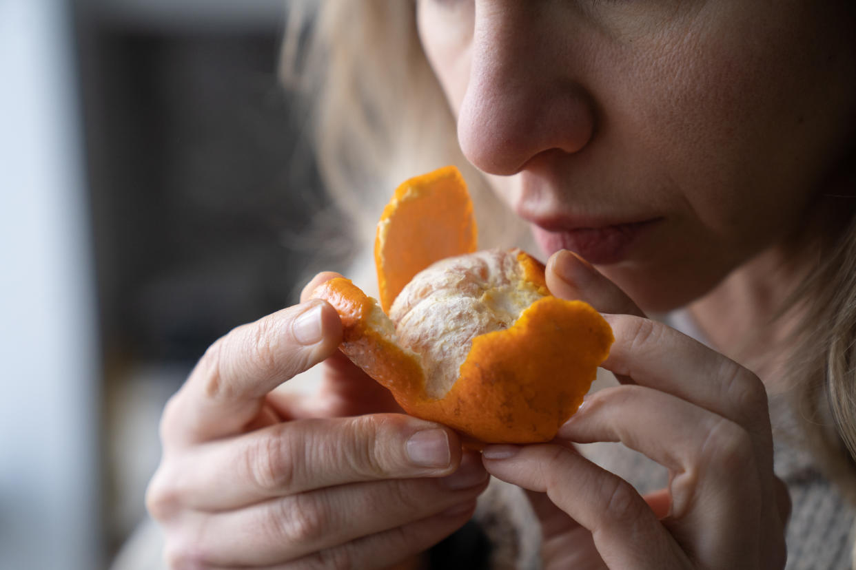 Sick woman trying to sense smell of fresh tangerine orange, immune system has symptoms of Covid-19, corona virus infection - loss of smell and taste, standing at home. One of the main signs of the disease.