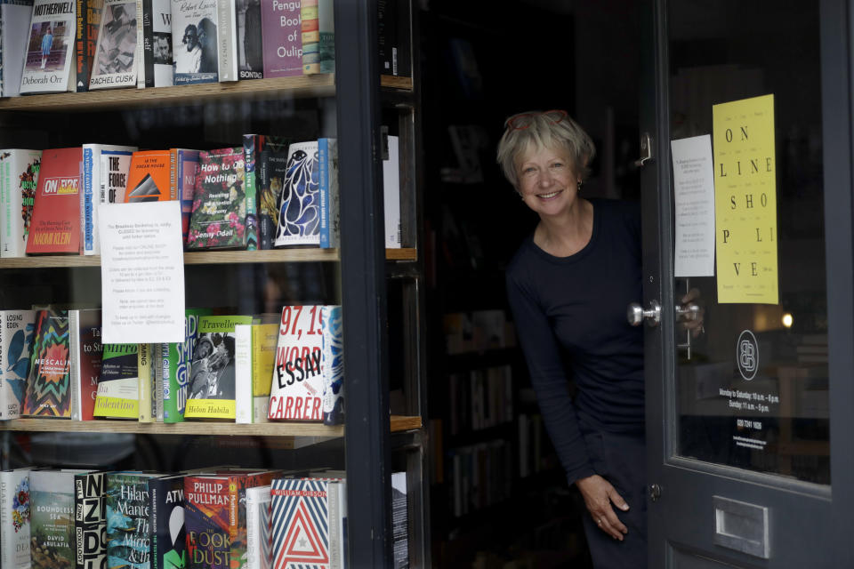 Jane Howe, owner of the Broadway Bookshop, poses for a photo in the doorway of her shop on Broadway Market in Hackney, east London on June 28, 2020. Before the coronavirus, Howe never saw the need for a website. Shoppers would pack the tidy shop on weekends, with more often waiting outside, drawn by the store’s personalized service. She finally launched a website in mid-June and loyal customers have been placing orders, but sales are far below what they were before the pandemic. (AP Photo/Matt Dunham)