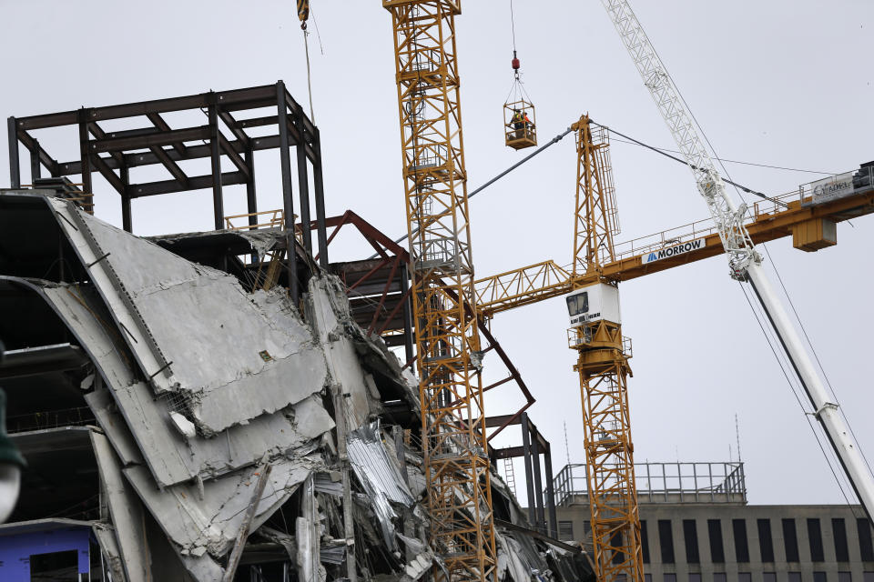 Workers in a bucket hoisted by a crane begin the process of preparing the two unstable cranes for implosion at the collapse site of the Hard Rock Hotel, which underwent a partial, major collapse while under construction last Sat., Oct., 12, in New Orleans, Friday, Oct. 18, 2019. Plans have been pushed back a day to bring down two giant, unstable construction cranes in a series of controlled explosions before they can topple onto historic New Orleans buildings, the city's fire chief said Friday, noting the risky work involved in placing explosive on the towers. (AP Photo/Gerald Herbert)