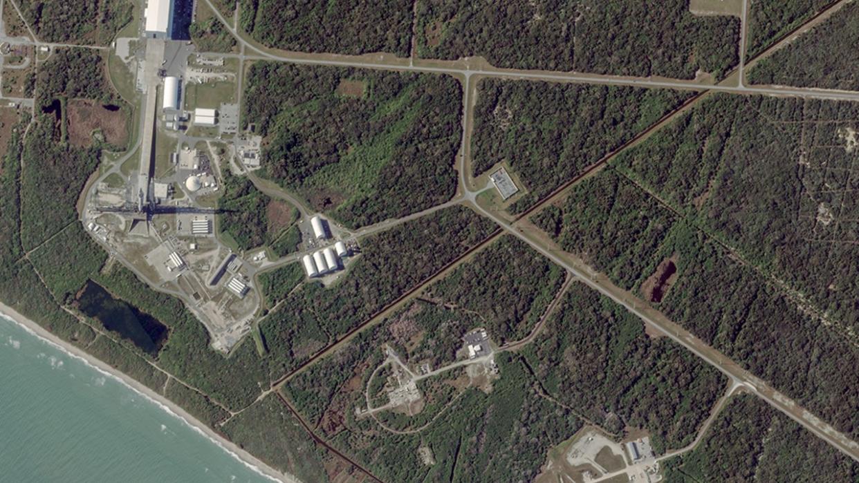  A satellite view of a rocket standing on a launch pad, surrounded by green vegetation. 