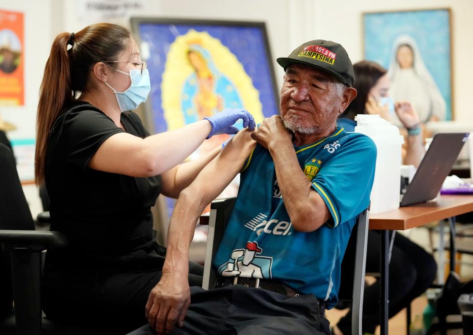 Antonio Rodriguez rolls his sleeve up before getting his COVID-19 booster from medical assistant Jessica Lopez during a clinic at Promise Arizona's office in Phoenix.