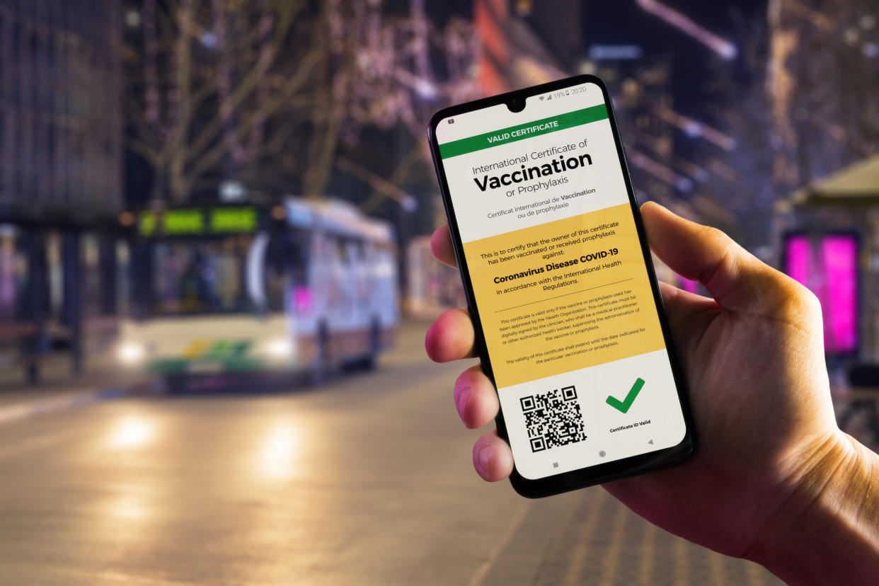 Smartphone displaying a valid digital vaccination certificate for COVID-19 in male's hand, downtown and city bus in background. Vaccination, immunity passport, health and surveillance concepts