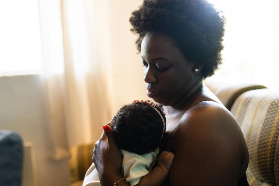 Seated woman gently cradles and looks at her baby in a peaceful room