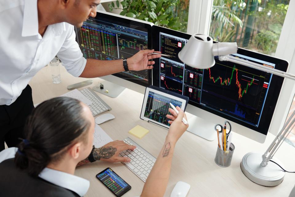 Team of serious stockbrokers having conversation in office with multiple display screens and analyzing stock trends