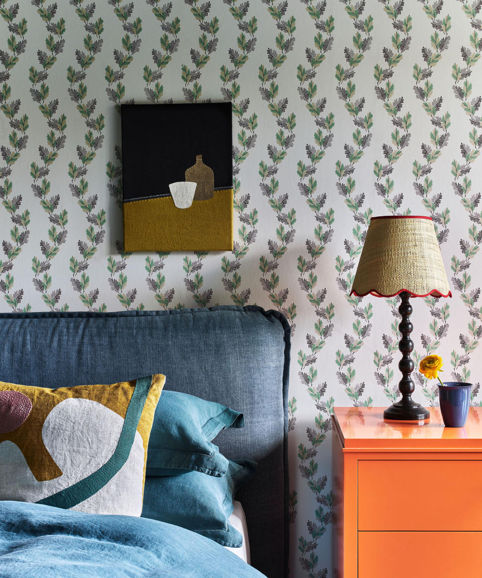 <p> This pretty and delicate oak leaf botanical print from Common Room is a wonderful example of a small scale wallpaper that feels perfectly suited to a bedroom.  </p> <p> It has a classic, timeless feel, which when combined with a relaxed denim blue linen upholstered bed and vibrant orange lacquer bedside cabinet makes for a truly unique and fresh look.  </p> <p> The gentle, pared-back design allows the bold use of colour elsewhere to not overwhelm the room. All the different bedroom color ideas work happily together in harmony.  </p> <p> The tactile nature of the textile artwork, contemporary applique cushion, linen headboard and woven lampshade all add to the welcoming and cosy feel. </p>