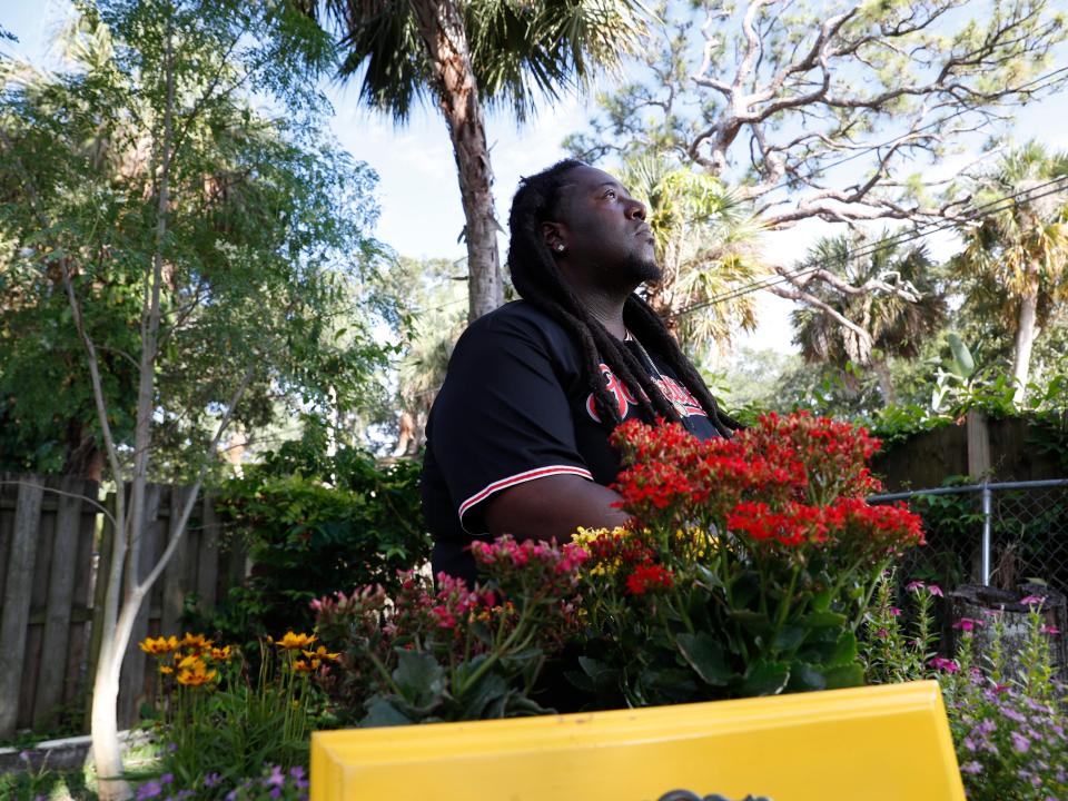 Corey "Goo" Paul wears a jersey and looks up toward the sky while standing in his garden full of plants.