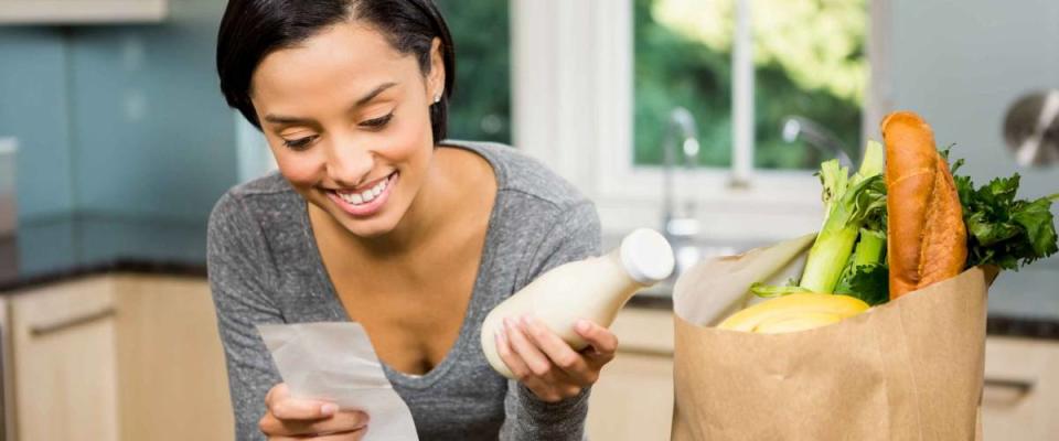 Smiling brunette holding receipt and milk in the kitchen