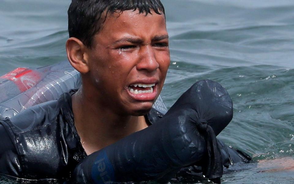 A Moroccan boy cries as he swims using bottles as a float, near the fence between the Spanish-Moroccan border, after thousands of migrants swam across the border, in Ceuta, Spain - Jon Nazca/REUTERS