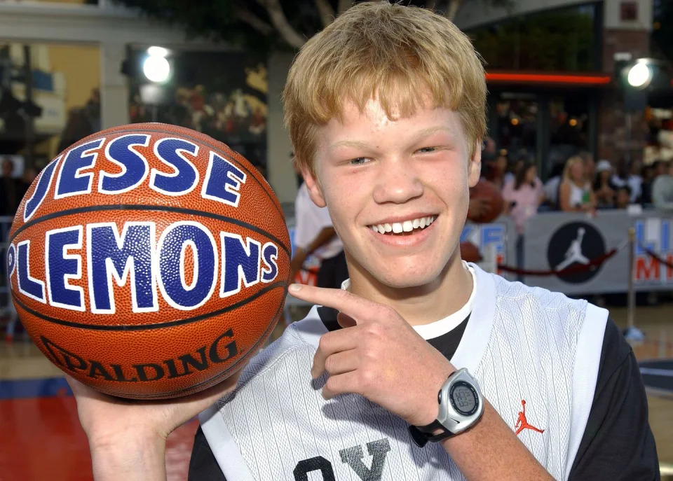 jesse plemons smiles at the camera and points one finger at a basketball he holds in his other palm that has his name on it