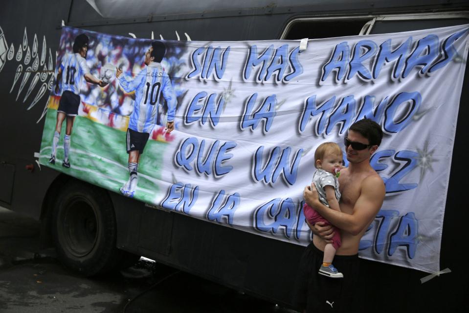 An Argentinian fan carrying a baby stands in front of a banner of Lionel Messi as he waits amongst others at a tent and motorhomes park at the Terreirao do Samba for Sunday's World Cup final match between Argentina and Germany in Rio de Janeiro