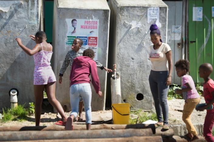 A woman fills a bucket from a communal tap as children play (AFP Photo/RODGER BOSCH)