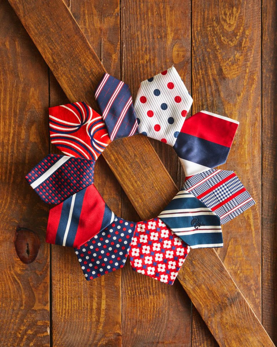 a wreath made from vintage red white and blue ties hung on a brown wood door