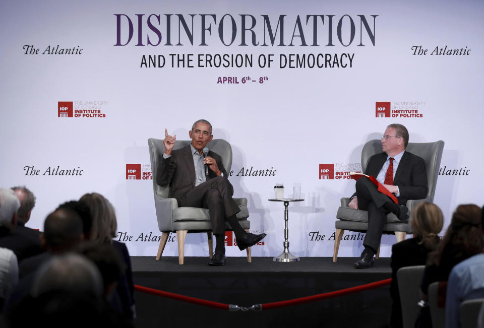 Former President Barack Obama, points his index finger in the air, in conversation with Jeffrey Goldberg, in front of an audience, with the title of the conference, Disinformation and the Erosion of Democracy, posted on the screen behind them.