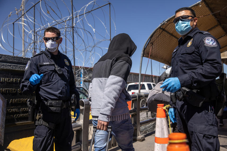 Asylum seekers pass U.S. Customs and Border Protection officers while crossing an international bridge from Mexico into the United States on March 17, 2021, in Ciudad Juarez, Mexico. (John Moore / Getty Images)