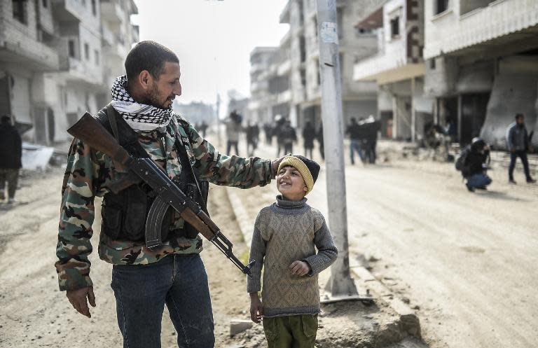 Un combatiente kurdo camina con su hijo por el centro de la estratégica localidad kurdosiria de Kobane.