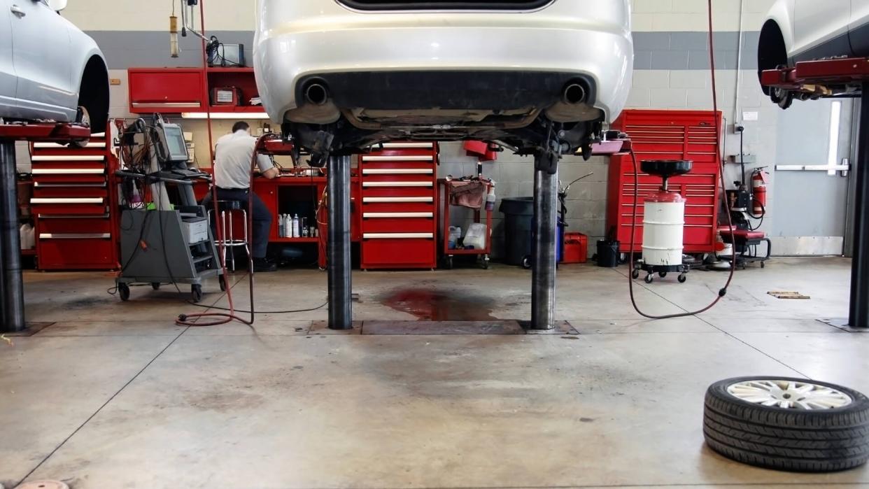 The interior of a car dealership repair facility, shows two cars on hoists.