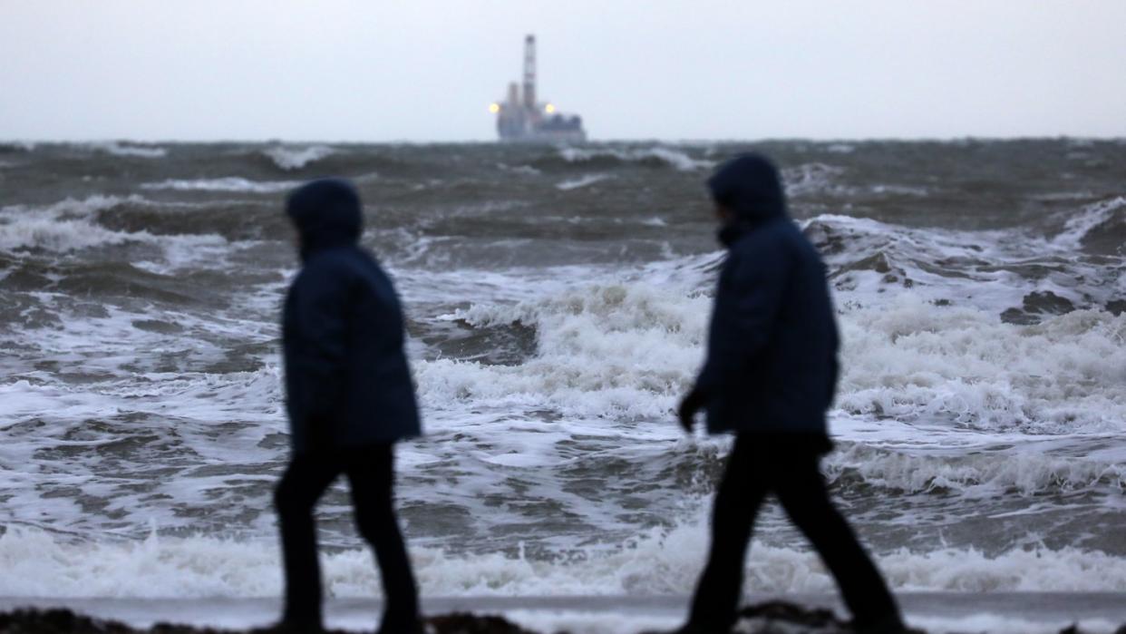 Spaziergänger sind in Warnemünde an der aufgewühlten Ostsee unterwegs. Foto: Bernd Wüstneck