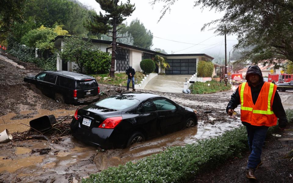 Cars are stranded in a mudslide as a man attempts to clear away debris left behind by the storm