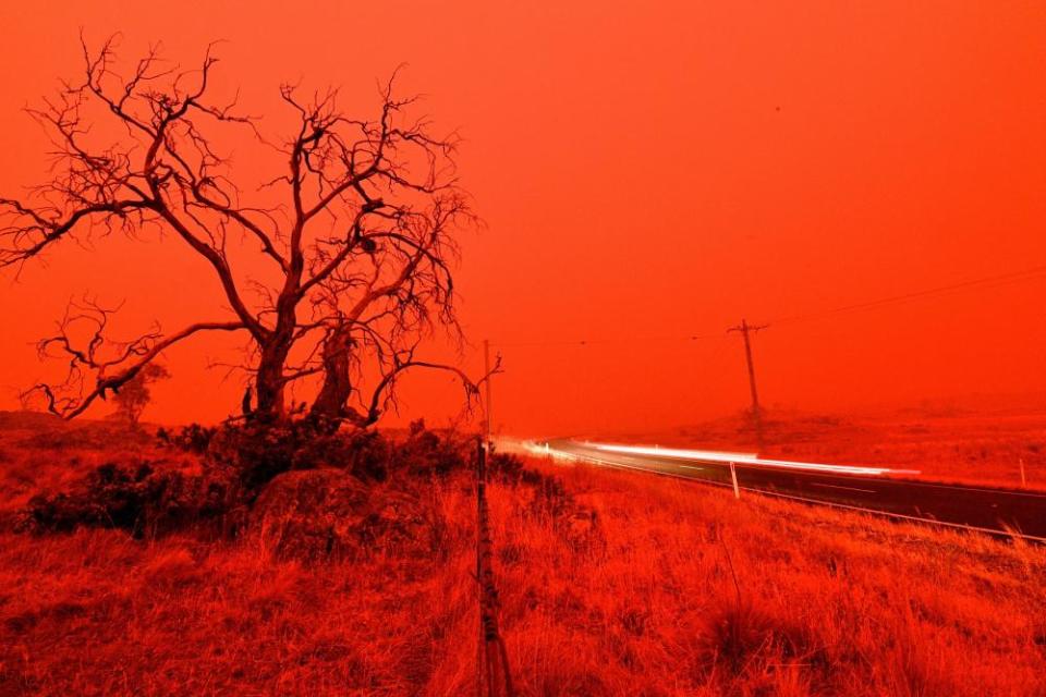 A long exposure picture shows a car commuting on a road as the sky turns red from smoke of the Snowy Valley bushfire on the outskirts of Cooma.