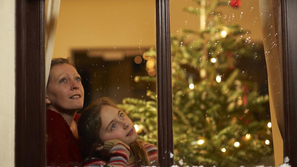 girl and mother gazing out of window at christmas