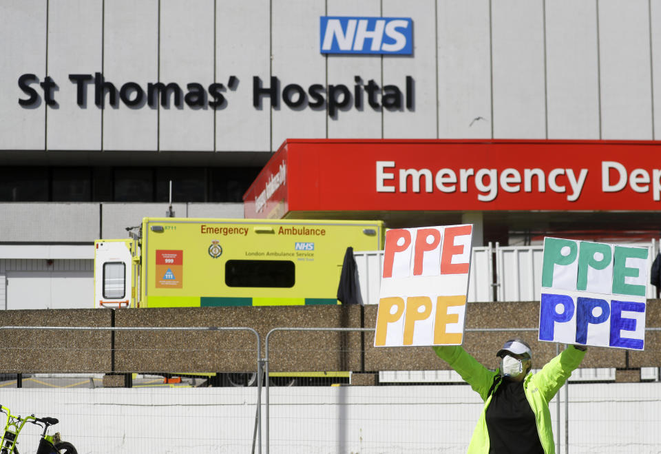 A woman holding up signs (PPE-Personal Protection Equipment) stands outside St Thomas' Hospital in central London as British Prime Minister Boris Johnson is in intensive care fighting the coronavirus in London, Tuesday, April 7, 2020. Johnson was admitted to St Thomas' hospital in central London on Sunday after his coronavirus symptoms persisted for 10 days. Having been in hospital for tests and observation, his doctors advised that he be admitted to intensive care on Monday evening. The new coronavirus causes mild or moderate symptoms for most people, but for some, especially older adults and people with existing health problems, it can cause more severe illness or death.(AP Photo/Kirsty Wigglesworth)