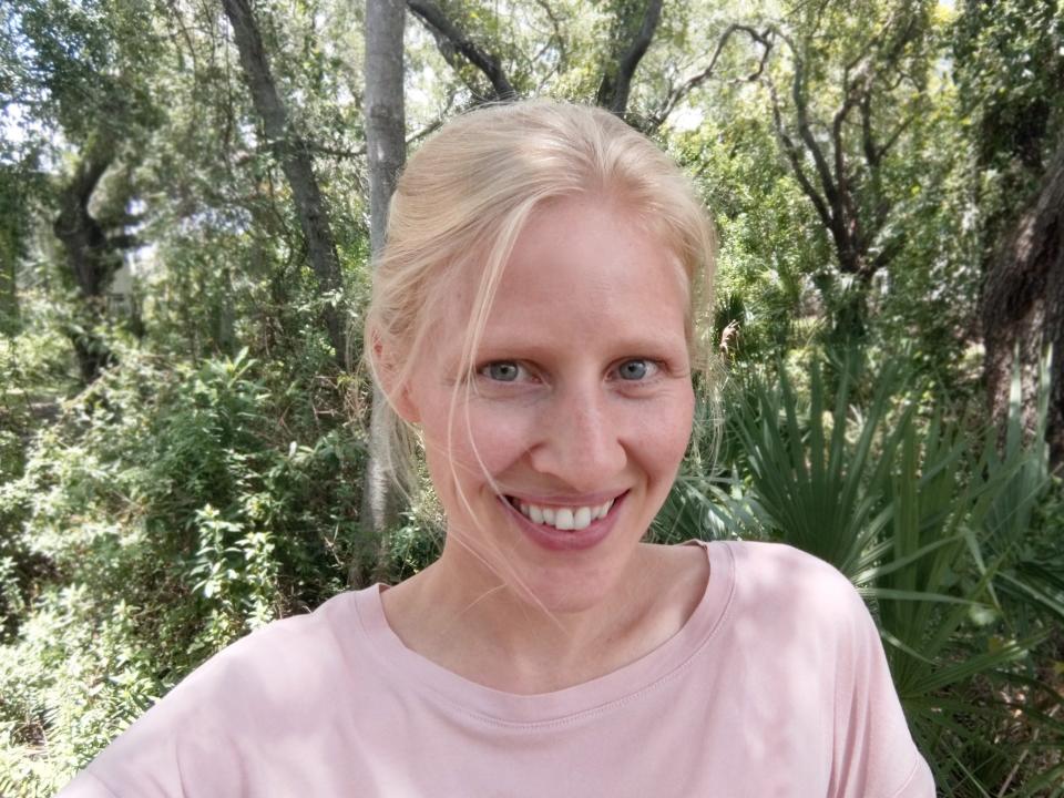 A selfie of a woman with blonde hair and a light pink t-short smiling at the camera.